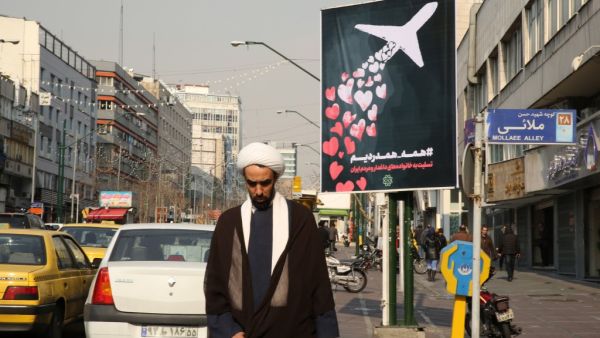 An Iranian cleric walks past a poster honouring the victims of a Ukrainian passenger jet accidentally shot down in the capital last week, in front of the Amirkabir University in the capital Tehran, on January 13, 2020.  (AFP/ File Photo)