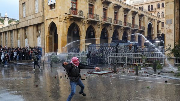 An anti-government protester throws a rock at security forces as they fire water cannon from behind a barrier during clashes in the central downtown district of the Lebanese capital Beirut near the parliament headquarters on January 18, 2020. ANWAR AMRO / AFP
