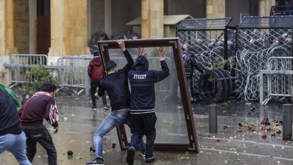 Anti-government protesters use a window as a makeshift shield as they confront security forces from behind a barbed-wire and metal fence barrier during clashes in the central downtown district of the Lebanese capital Beirut near the parliament headquarters on January 18, 2020. ANWAR AMRO / AFP