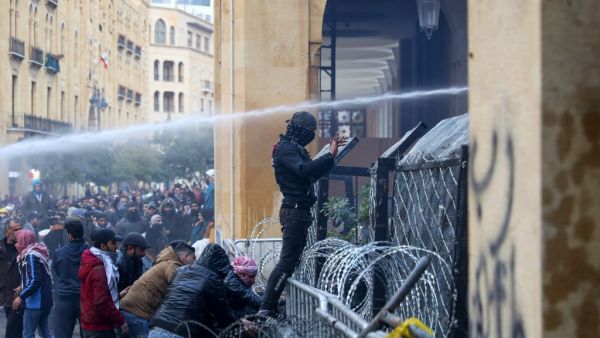 An anti-government protester displays the middle-finger gesture as security forces spray water cannon at demonstrators during clashes in the central downtown district of the Lebanese capital Beirut near the parliament headquarters on January 18, 2020. Anwar AMRO / AFP