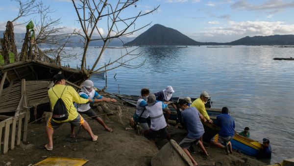 A group of fishermen haul a boat from the water as they make repairs to their operations affected by the eruption of the Taal volcano, in Buso Buso on January 20, 2020. Ed JONES / AFP
