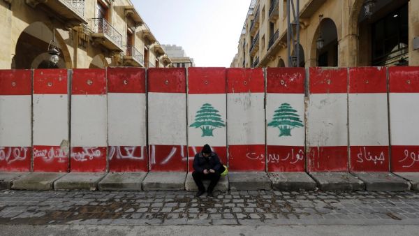 A man sits in front of a wall of cement blocks, set up by Lebanese security forces to bar a street leading to the country's parliament building in the capital Beirut's downtown district, on January 24, 2020. JOSEPH EID / AFP