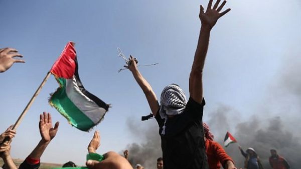 Palestinian demonstrators wave their national flag and shouts slogans against Israeli security forces during a protest on the Israel-Gaza border in the northern Gaza Strip on April 6, 2018. (AFP/Mohammed Abed)