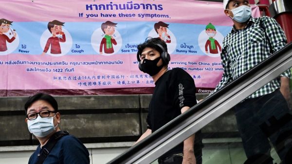 People wearing protective facemasks walk past a government health advisory campaign on the coronavirus infection prevention at a city commuter train station in Bangkok, on February 1, 2020. AFP