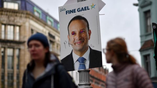 Pedestrians walk past a defaced campaign poster featuring Ireland's Prime Minister and leader of the Fine Gael party, Leo Varadkar as they walk along a street in Dublin on February 7, 2020, on the eve of the country's General Election. Ireland on Friday entered the final day of campaigning before this weekend's election, as polls predicted a historic three-way fight for control of the next government. Prime Minister Leo Varadkar, of the Fine Gael party, was canvassing in the western town of Ennis while Fian
