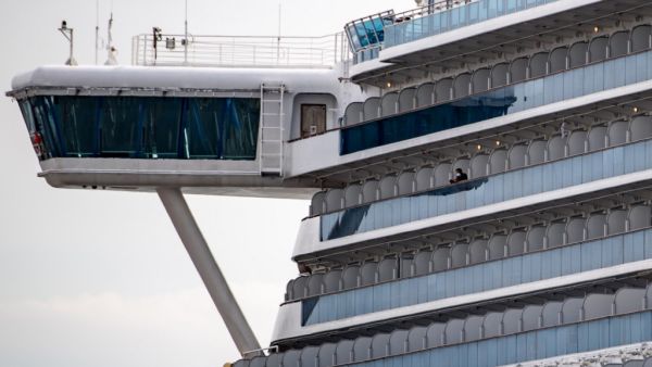 A passenger wearing a face mask looks out from the cabin of the Diamond Princess cruise ship, in quarantine due to fears of new COVID-19 coronavirus, at Daikoku pier cruise terminal in Yokohama on February 20, 2020. Two former passengers of the coronavirus-wracked Diamond Princess have died, local media reported, as fears mount about those who have left the ship after testing negative for the virus. Philip FONG / AFP