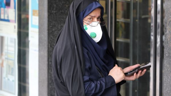 A woman wears a protective mask while using a smartphone as she stands along the side of a street in the Iranian capital Tehran on February 24, 2020. Iran's government vowed on February 24 to be transparent after being accused of covering up the deadliest coronavirus COVID-19 outbreak outside China as it dismissed claims the toll could be as high as 50. The authorities in the Islamic republic have come under mounting public pressure since it took days for them to admit to "accidentally" shooting down a Ukra