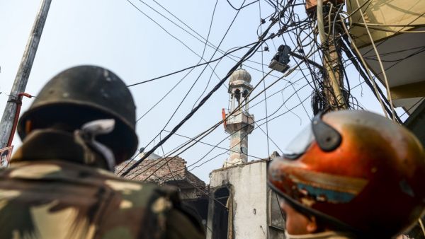 Security personnel stand guard on a road as a Hindu religious flag is seen on a minaret (C) of a burnt-out mosque following clashes between people supporting and opposing a contentious amendment to India's citizenship law in New Delhi on February 26, 2020. Four more people have died in some of the worst sectarian violence in decades in New Delhi, a hospital source told AFP, which takes the death toll from several days of rioting to 17. Sajjad HUSSAIN / AFP