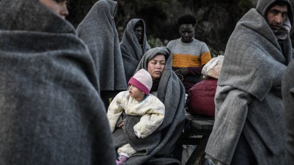 Migrants and refugees who arrived from Turkey to the Greek island of Lesbos on March 5, try to keep warm as they gather in the yard of a small church where they have spent the rainy night near Skala Sykamnias on March 6, 2020. A group of 42 refugees and migrants weave through coast guard patrols and arrived on the shores of Lebos during the evening of March 5. LOUISA GOULIAMAKI / AFP