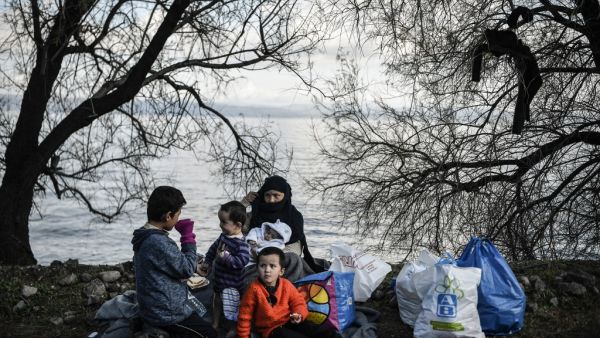 A family sits on a blanket near the yard of a small church where they spent the night after arriving last night near Skala Sykamnias on the Greek island of Lesbos on March 6, 2020. A group of 42 refugees and migrants managed to by pass coast guard patrols and landed on the shores of Lesbos in the evening of March 5. LOUISA GOULIAMAKI / AFP