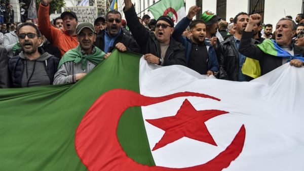 People chant slogans as they wave a large Algerian national flag during a weekly anti-government demonstration in the capital Algiers on March 6, 2020. Protests against cronyism have continued in Algeria despite former president Abdelaziz Bouteflika's resignation and the election of a new president in December 2019. RYAD KRAMDI / AFP