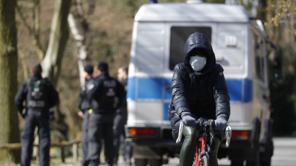 A cyclist wearing a protective mask bikes past a police patrol at the Tiergarten park in Berlin on March 23, 2020, amid the new coronavirus COVID-19 pandemic. Odd ANDERSEN / AFP