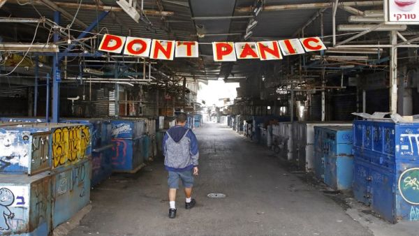 A man passes under a "Don't Panic" banner hanging at the entrance of Shuk HaCarmel (Caramel) market in the Israeli coastal city of Tel Aviv on March 24, 2020 after Israel barred residents from leaving home for non-essential reasons and stopped night-time public transport, tightening already strict measures to fight the spread of coronavirus. JACK GUEZ / AFP