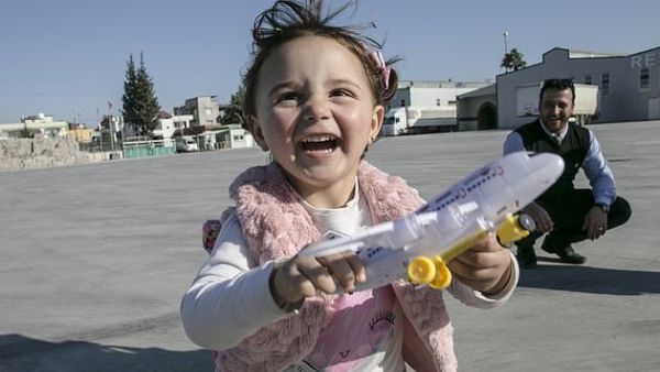 Syrian girl Salwa laughs with her new toys at the Cilvegozu border crossing in Hatay, Turkey (Dailymail)