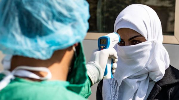 A health care worker checks the temperature of a woman arriving by bus to Syrian Kurdistan (Rojava) from the Kurdistan Region to test for the coronavirus, Feb. 26, 2020 (Photo: AFP/Delil Souleiman)