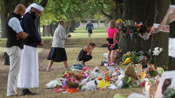 People on Tuesday stand next to floral tributes placed across the road from the Al Noor Mosque in Christchurch, New Zealand, where dozens of worshippers were gunned down last week. (Marty Melville/AFP/Getty Images)