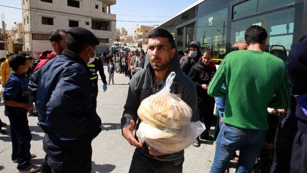 People queue to buy subsidised bread from a municipal bus in the Marka suburb in the east of Jordan's capital Amman on March 24, 2020, as the kingdom announced it would deliver bread and water supplies after the government decided to indefinitely extend a curfew amidst efforts to contain COVID-19 coronavirus disease. Jordan imposed a curfew after citizens failed to heed instructions not to leave home except for emergencies, and it has deployed the army to enforce the measure. A fleet of 190 buses chartered 