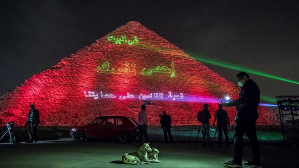 A man takes pictures of dogs in front of the Great pyramid of Kheops at the Giza plateau outside the Egyptian capital Cairo where a laser projection writes "Stay at home, stay safe. Thanks to those keeping us safe" on March 30, 2020, amid the spread of the COVID-19 infection, caused by the novel coronavirus. Khaled DESOUKI / AFP