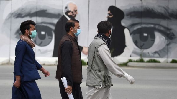 Men wearing facemasks as a precautionary measure against the COVID-19 novel coronavirus walk past a wall painted with images of US Special Representative for Afghanistan Reconciliation Zalmay Khalilzad (L) and Taliban co-founder Mullah Abdul Ghani Baradar (R), in Kabul April 5, 2020. WAKIL KOHSAR / AFP