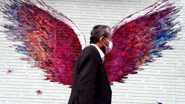 A man wearing a face mask amid concerns over the spread of COVID-19 coronavirus walks past a graffiti of wings in Tokyo on April 7, 2020. Japan's Prime Minister Shinzo Abe will on April 7 declare a state of emergency in parts of the country, including Tokyo, over a spike in coronavirus infections. Behrouz MEHRI / AFP