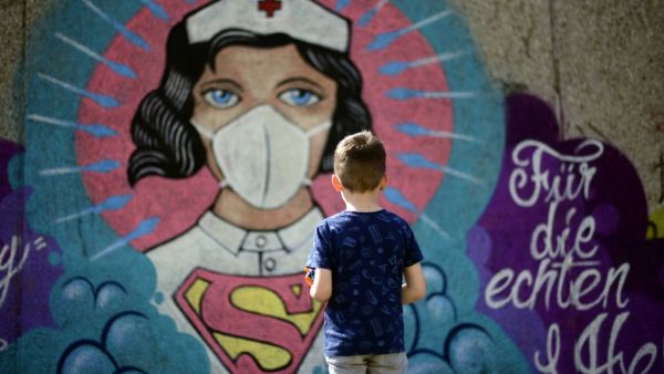 A boy stands in front of a graffiti painted by artist Kai 'Uzey' Wohlgemuth featuring a nurse as Superwoman on a wall in Hamm, western Germany, on April 8, 2020 refering to the spread of the novel coronavirus COVID-19. Ina FASSBENDER / AFP