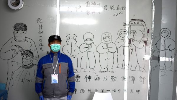 A security personnel stands in front of coronavirus themed drawings seen on a wall at the Leishenshan Hospital that had offered beds for coronavirus patients in Wuhan, in China’s central Hubei province on April 11, 2020. Noel Celis / AFP