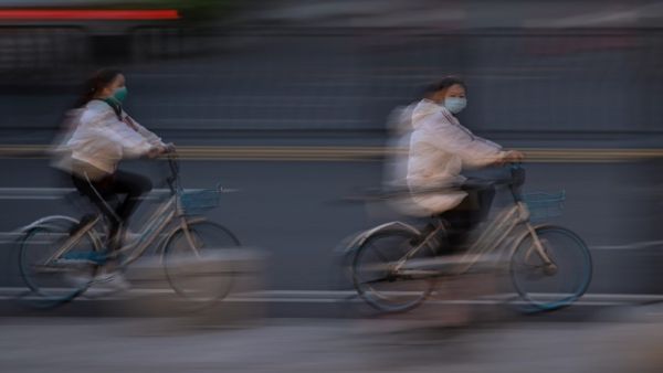 Women wearing face masks ride bicycles on a street in Wuhan, in China's central Hubei province on April 11, 2020. Hector RETAMAL / AFP