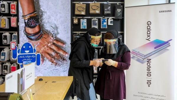 Iranian women, wearing personal protective equipment, look at a cell phone at a shop in Mashhad on April 11, 2020, amid the coronavirus (COVID-19) pandemic.  AFP/File