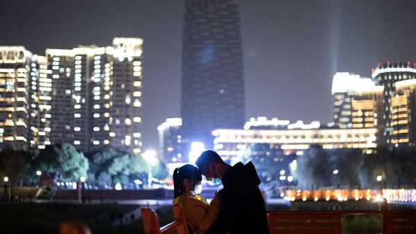 A couple wearing a facemask cuddles along a park at the Yangtze river in Wuhan, in China's central Hubei province early on April 12, 2020. NOEL CELIS / AFP