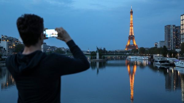 A man takes pictures of the Eiffel tower and its reflection on the Seine river, in Paris, on April 12, 2020, on the 27th day of a strict lockdown aimed at curbing the spread of the COVID-19 pandemic, caused by the novel coronavirus. Ludovic MARIN / AFP