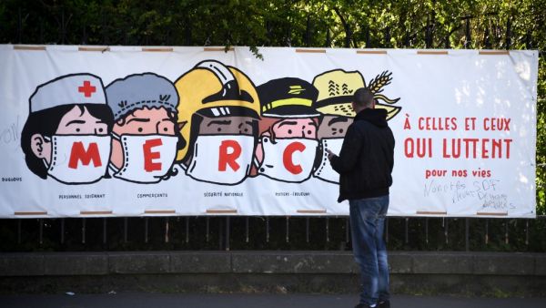 A man looks at a poster thanking the healthcare personnel, shopkeepers, the French national security, the post office staff members and farmers, in Paris, on April 14, 2020, on the twenty-nineth day of a lockdown in France to stop the spread of the COVID-19, (the novel coronavirus). FRANCK FIFE / AFP