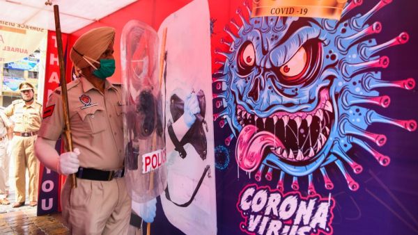A policeman poses for photos inside a 'disinfectant tunnel' next to a poster depicting the COVID-19 coronavirus during an event in Amritsar on April 16, 2020. Narinder NANU / AFP