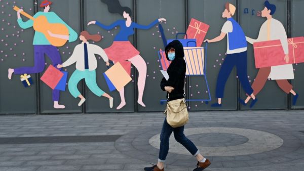 A woman wearing a face mask walks past a mall in Beijing on April 21, 2020. WANG ZHAO / AFP