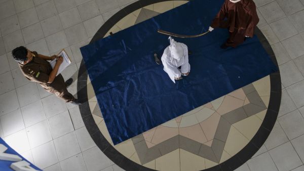 A woman (C) is whipped by the religious police in a public building in Banda Aceh on April 21, 2020, as punishment after he was caught in close proximity with a man who is not her husband in a hotel. AFP