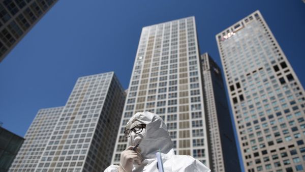 A worker, wearing a protective suit amid concerns about the COVID-19 coronavirus, waits to check the temperature of drivers at the entrance to the car park of a commercial complex in Beijing on April 22, 2020. GREG BAKER / AFP