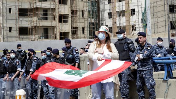 An anti-government protester waves the national flag as security forces wearing masks stand guard during a convoy protest in front of Mohammad Al-Amin mosque in the Lebanese capital Beirut on April 22, 2020, amid an economic crisis exacerbated by the coronavirus pandemic. (AFP/File)