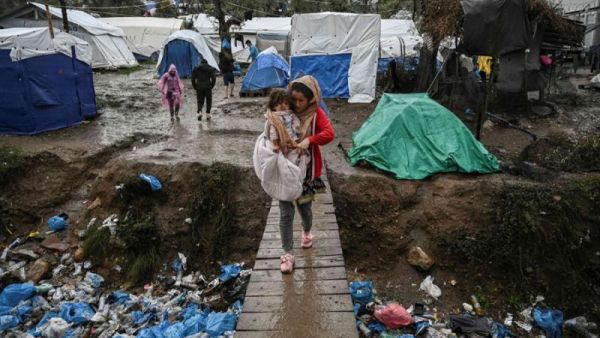 A woman carries her child as she crosses a wooden bridge in the refugee camp of Moria, on the island of Lesbos, November 26. (AFP)