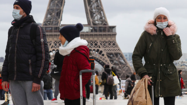 People wear protective facemasks as they walk in front the Eiffel Tower, in Paris on March 12, 2020 | Ludovic Marin/AFP via Getty Images