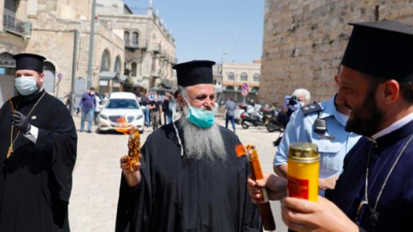 Greek Orthodox priests hold candles lit from the Holy Fire in the church of the Holy Sepulchre [Ahmad Gharabli/AFP]