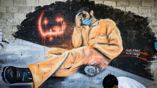 A youth, wearing a protective mask, walks past a mural reading "We are tired" in the Lebanese northern city of Tripoli on April 28, 2020. Lebanon is facing its worst economic crisis since the 1975-1990 civil war, now compounded by a nationwide lockdown to stem the spread of the coronavirus. The Lebanese pound has lost more than half of its value, and prices have soared.This is the case across the country, but Tripoli has been especially hard hit because more than half of its population had already been livi