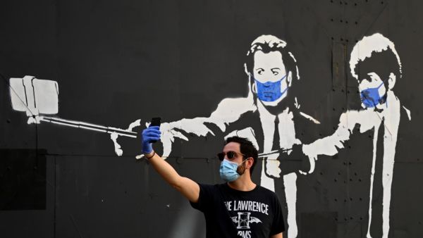A man takes a selfie photo in front of a stencil graffiti depicting US actors John Travolta and Samuel L. Jackson in their roles of "Vincent Vega" and "Jules Winnfield" in Quentin Tarantino's "Pulp Fiction", wearing face masks, in Madrid on May 3, 2020 amid a national lockdown to prevent the spread of the COVID-19 disease. Spain today counted another 164 coronavirus deaths, the lowest daily number in nearly seven weeks as the country begins to gradually lift its strict lockdown. The figures from the health 