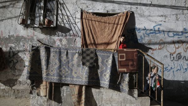 A Palestinian girl takes a peek from behind a curtain at her home's entrance as her sibling plays on the stairs, at al-Shati camp for Palestinians refugees, before sunset during the Muslim holy month of Ramadan, in Gaza City, on may 8, 2020, amid the COVID-19 pandemic. MOHAMMED ABED / AFP