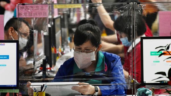 A local resident (C) wearing a face mask due the COVID-19 pandemic sits behind a plastic partition as she submits her tax documents at the Taipei National Taxation Bureau in Taipei on May 12, 2020. Sam Yeh / AFP