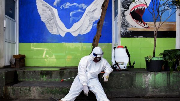 A health agency official, seen alongside his disinfectant dispenser, rests by the entrance to a public toilet as other colleagues (not pictured) conduct polymerase chain reaction (PCR) testing for the COVID-19 coronavirus at a bus station in Bandung, West Java, on May 13, 2020. TIMUR MATAHARI / AFP