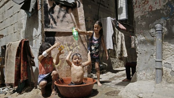 Palestinian girls pour water over a child's head to cool off during a heatwave at Bureij refugee camp in the central Gaza Strip, amidst the COVID-19 pandemic on May 19, 2020. (AFP)