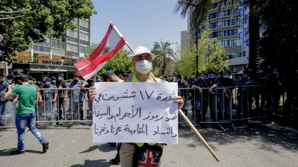 A Lebanese protester wearing a protective mask amid the COVID-19 pandemic, lifts a placard which reads "the October 17 revolution is against figures of crime and corruption. The resistance is our pride", as he demonstrates in the capital Beirut, on May 30, 2020. In parallel, anti-government protesters demonstrated on the same day demanding the implementation of United Nations resolutions including the disarmament of armed groups in the country. ANWAR AMRO / AFP