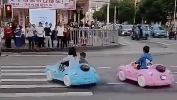 Social media footage captured the parent and her friend driving two play cars carrying the young boy on a crossroad with heavy traffic as pedestrians looked on. (Video Screenshot)
