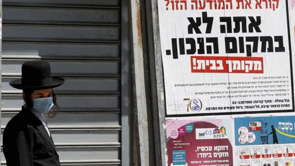 An ultra-Orthodox Jewish man wearing a mask walks past a sign reading in Hebrew "Reading this ad? You're not in the right place. (AFP/File Photo)