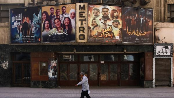 This picture taken early on May 24, 2020 shows a view of the historic Metro cinema theatre as a man walks past, along the commercial Talaat Harb street in the almost deserted city centre Egypt's capital Cairo, on the first day of Eid al-Fitr, the Muslim holiday which starts at the conclusion of the holy fasting month of Ramadan. Egypt had previously announced a lengthening of its night-time curfew and other measures to prevent large gatherings during the Eid al-Fitr holidays. One of the most important dates