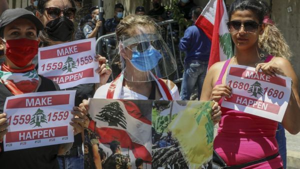 Lebanese anti-government protesters wearing protective gear amid the COVID-19 pandemic lift placards demanding the implementation of United Nations resolutions including the disarmament of armed groups in the country, during a demonstration in the capital Beirut, on May 30, 2020. ANWAR AMRO / AFP